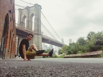 Man sitting on road against bridge in city