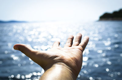 Close-up of hand against sea against clear sky