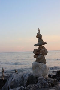 Statue on rock at sea shore against clear sky