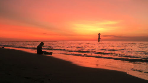 Silhouette woman sitting on beach against sky during sunset