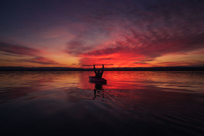 Silhouette man sitting on beach against sky during sunset