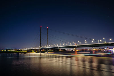 Illuminated bridge over river against sky at night