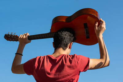 Rear view of man playing against blue sky