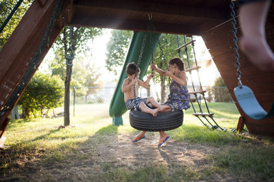 Playful siblings swinging on tire swing at playground