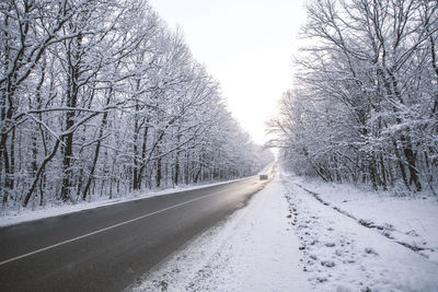 Road amidst snow covered trees against sky