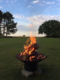 Firewood burning in pit on grassy field against sky