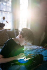 Teenager sitting on bed with sunlight working on tablet with stylus
