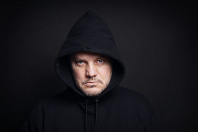 Portrait of serious man wearing hooded shirt against black background