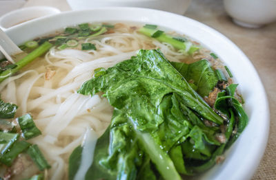 High angle view of a bowl of rice noodle soup and green vegetable on table
