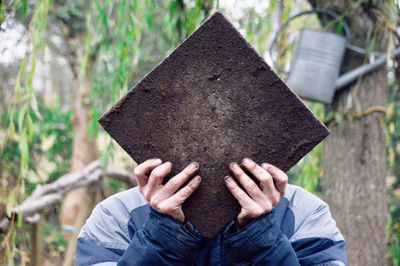 Man covering face with wood against trees