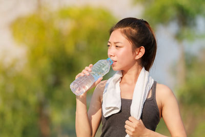 Young woman drinking water from bottle while standing outdoors