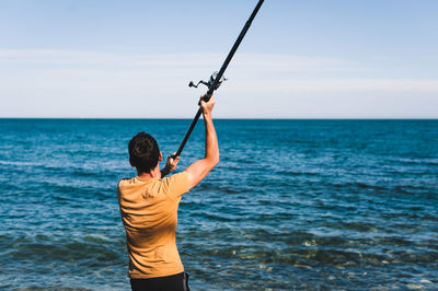 Rear view of man standing in sea against sky