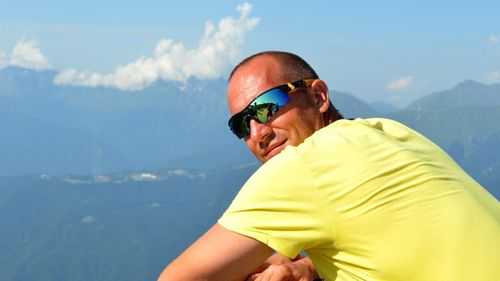 Portrait of man in sunglasses sitting against mountains during sunny day