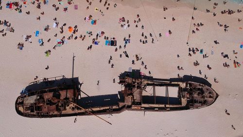 Drone view of people by abandoned ship at beach