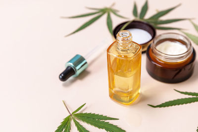 Cannabis cosmetic cream, face serum and hemp leaves over beige background. copy space.