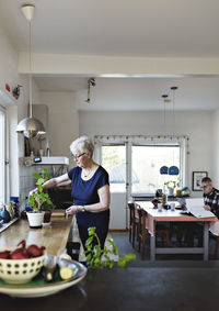 Retired senior woman watering potted plants on kitchen counter at home