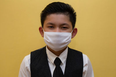 Portrait of boy wearing mask standing against yellow wall
