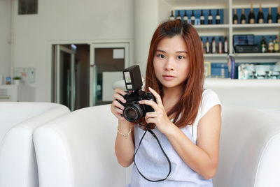 Portrait of young woman holding camera sitting at cafe