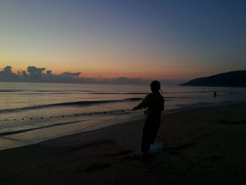 Silhouette man standing on beach against sky during sunset