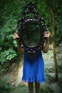 Woman holding mirror with reflection of trees while standing in forest