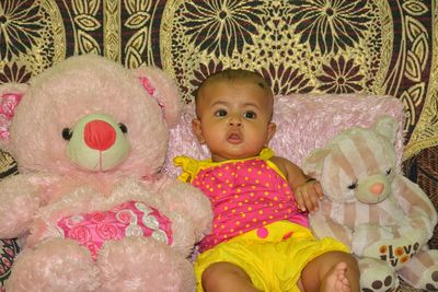 Cute baby girl lying by teddy bear on sofa at home