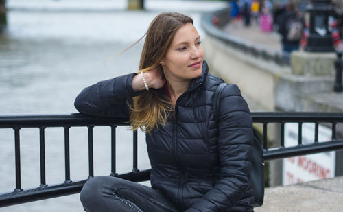 Portrait of young woman looking away while sitting on railing