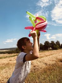 Boy playing with balloons on the field against the sky