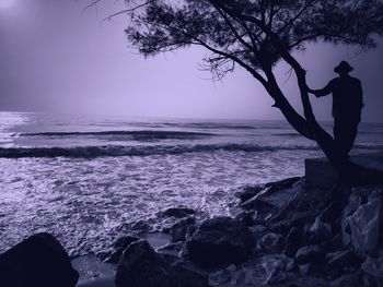 Silhouette man on rock at beach against sky