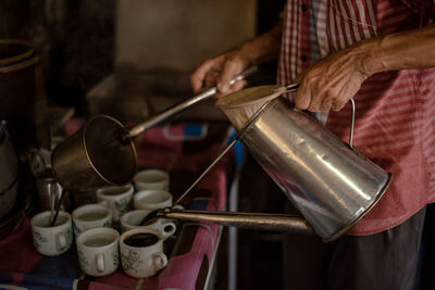 Midsection of man pouring tea in cups at table