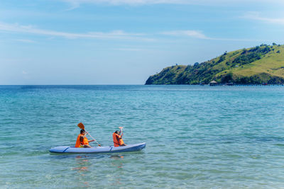 Friends kayaking on sea against sky