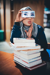 Woman covering eyes with mobile phone at table