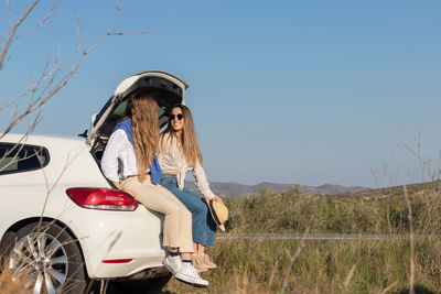 Friends sitting in a white car boot, taking a break from driving while on a spring road trip