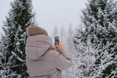 Girl taking pictures of winter forest using phone