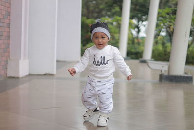 Cute and adorable toddler with a cute smile while standing on the floor in a sporty white costume