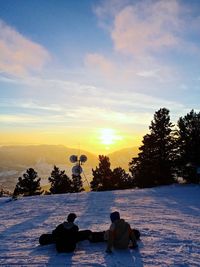 Rear view of man sitting on bench at sunset