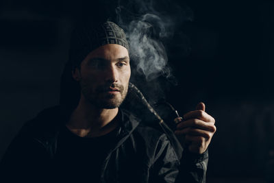 Portrait of young man smoking cigarette against black background