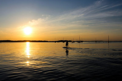 Rear view of silhouette man paddleboarding on lake against orange sky