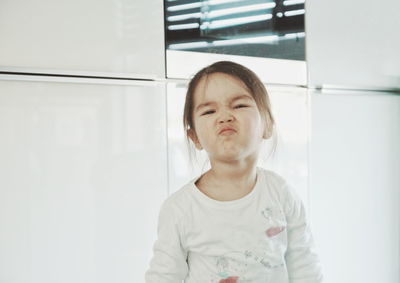 Portrait of girl making a face while standing in kitchen at home