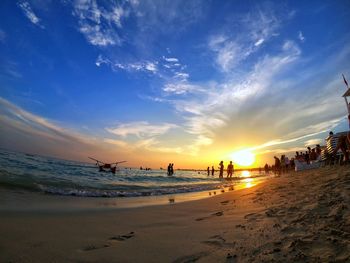 Group of people on beach against sky during sunset