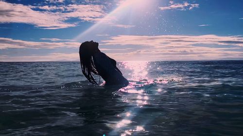 Silhouette person in sea against sky during sunset