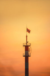 Lighthouse by sea against orange sky