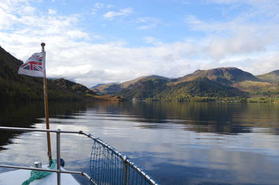 Sailing boat on calm lake against mountains and sky