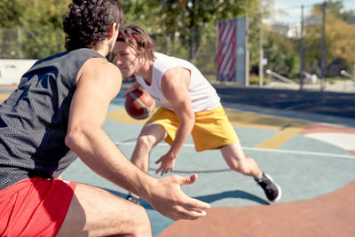 Male friends playing basket ball in sport court