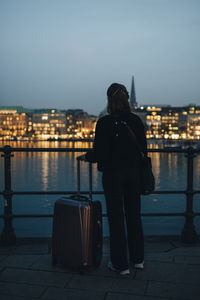 Rear view of businesswoman with luggage looking at illuminated city