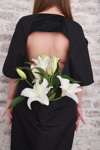 Fashion details, bouquet of white lilies is hidden in the dress of a girl, who is standing backwards