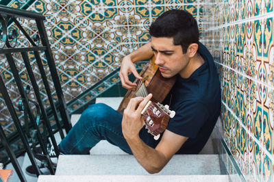 Focus man playing guitar sitting on a staircase with beautiful tiles.