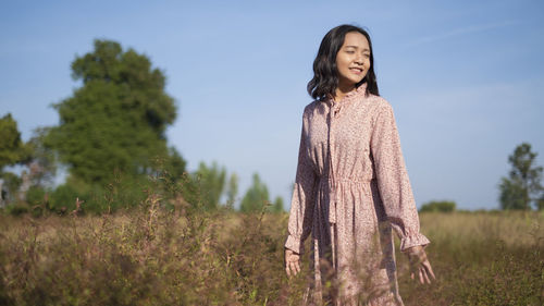 Woman standing by tree on field against sky