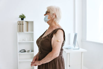 Side view of woman standing against curtain at home