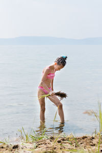  girl in a bathing suit fanns her thigh with a broom of grass while imitating bath procedures
