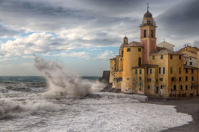 Buildings by sea against cloudy sky